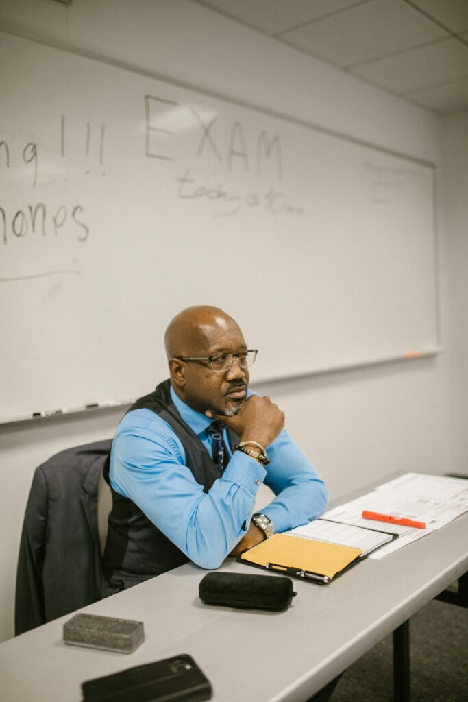 pexels-photo-7092419-7092419 Mature teacher sitting at desk proctoring an examination in a classroom.